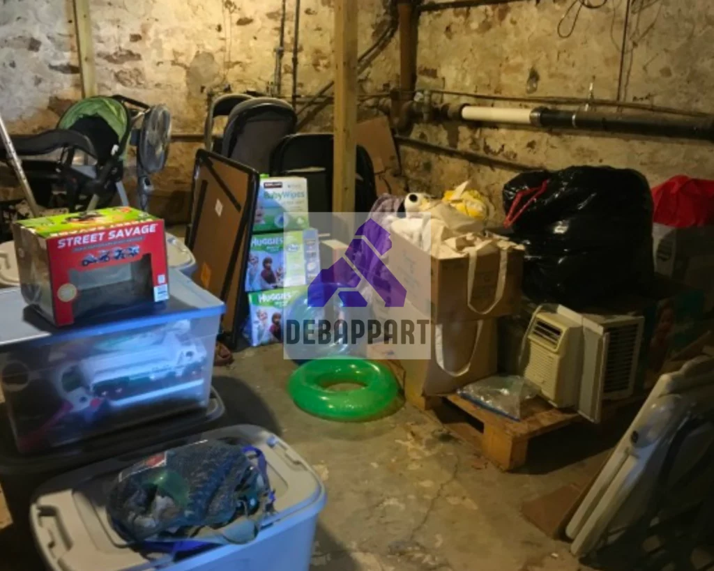 Cave encombrée jusqu’à la voûte : bacs de rangement, valises, cartons et matériel entassés
